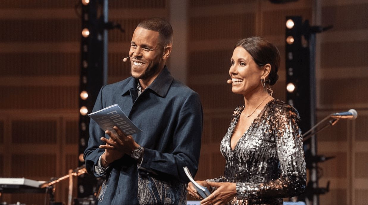 Mathias Zanka and a female presenter smiling on stage, holding microphones in a well-lit venue.