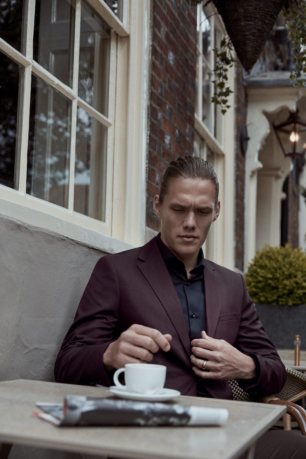 Jannik Vestergaard seated at a café table, adjusting his suit, with a coffee cup nearby.
