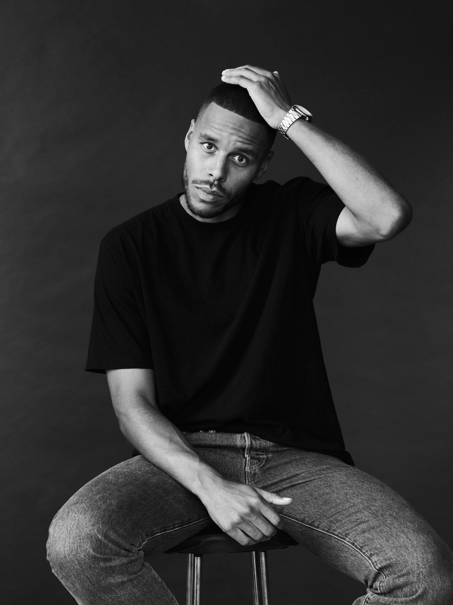 Mathias Zanka poses thoughtfully on a stool against a dark background.