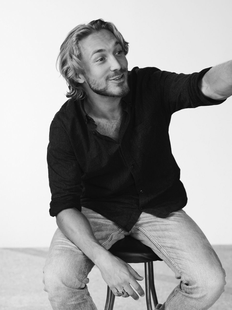 Andreas Jessen seated on a stool, smiling and gesturing in a bright, minimalistic setting.
