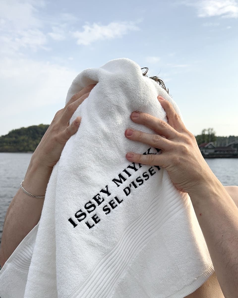 Rasmus Brohave holds a towel to his face by a serene body of water.