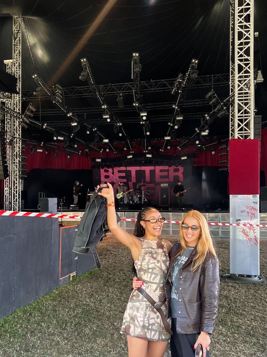 Bathsheba and a friend pose happily in front of a concert stage.