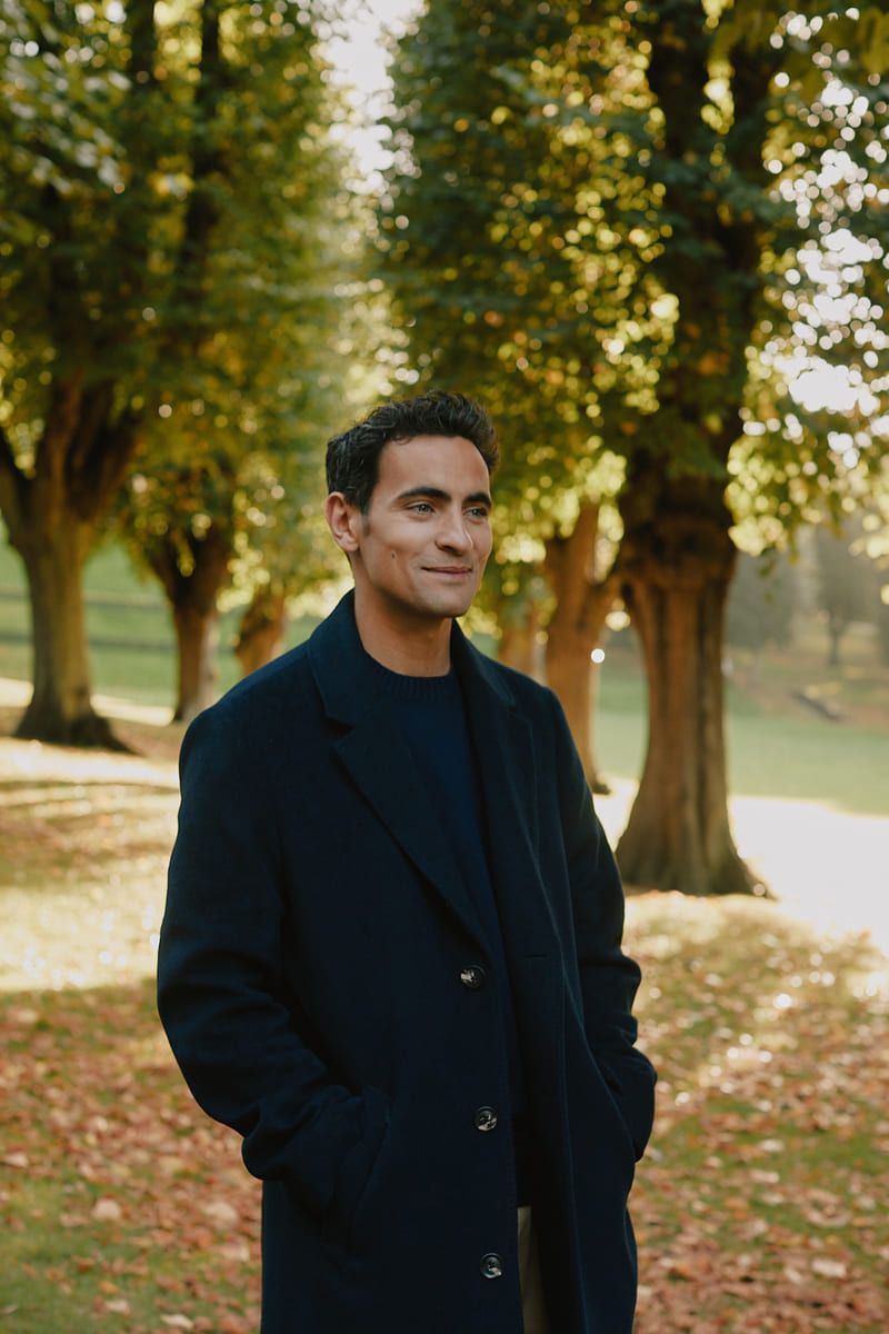 Jonathan Harboe stands in a sunlit park surrounded by trees and autumn leaves.