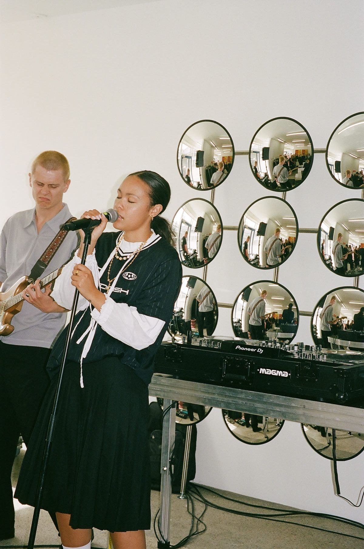 Bathsheba performs while a musician plays guitar, surrounded by circular mirrors.